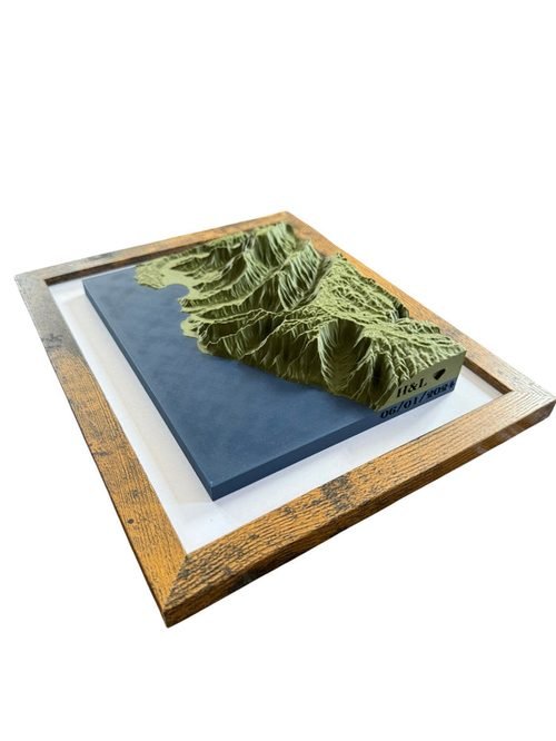 Green coastal terrain model with contrasting blue water in a wood-grain frame